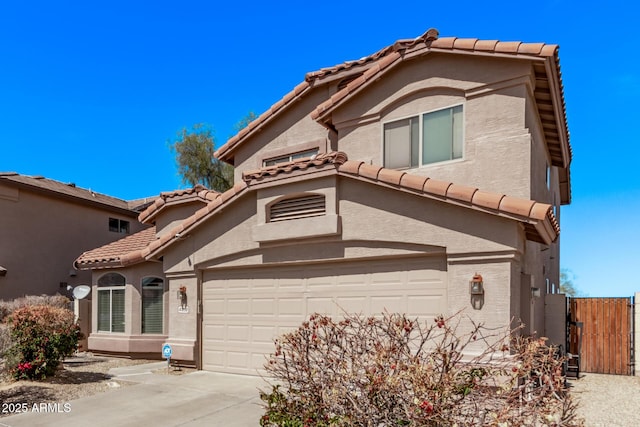 mediterranean / spanish home with concrete driveway, a tiled roof, a gate, and stucco siding