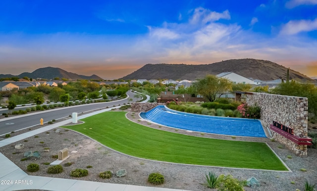 pool at dusk featuring a mountain view and a yard