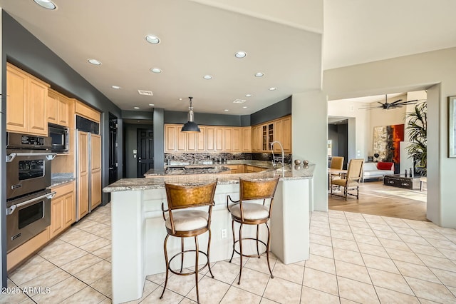 kitchen featuring ceiling fan, light stone countertops, double oven, kitchen peninsula, and black microwave