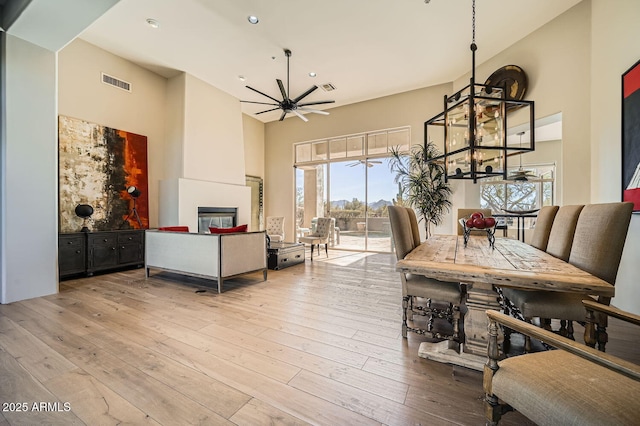 dining area with light wood-type flooring, a towering ceiling, a large fireplace, and ceiling fan