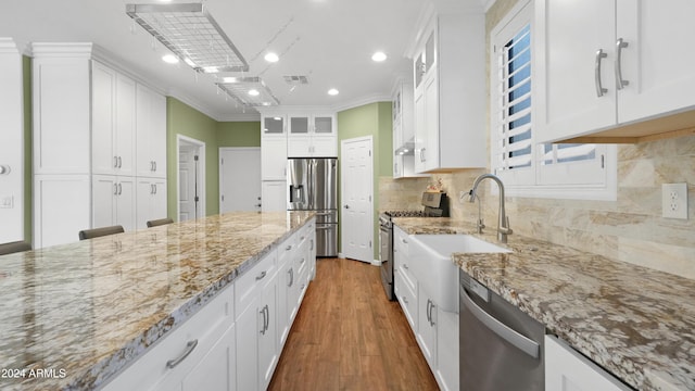 kitchen with stainless steel appliances, white cabinetry, light stone counters, ornamental molding, and dark hardwood / wood-style flooring