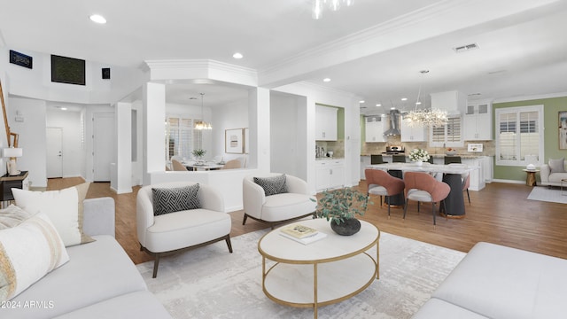 living room with a wealth of natural light, a notable chandelier, ornamental molding, and light hardwood / wood-style flooring