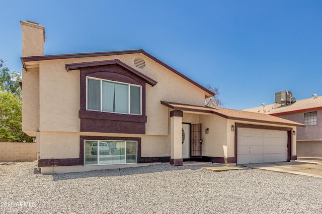 view of front of home featuring central AC, an attached garage, a chimney, driveway, and stucco siding