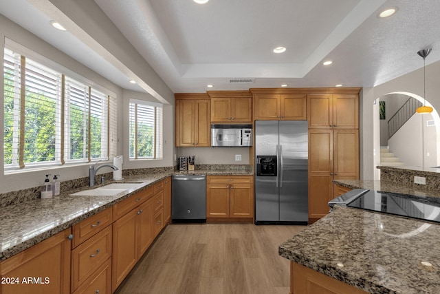 kitchen with hanging light fixtures, stainless steel appliances, dark stone counters, sink, and light wood-type flooring