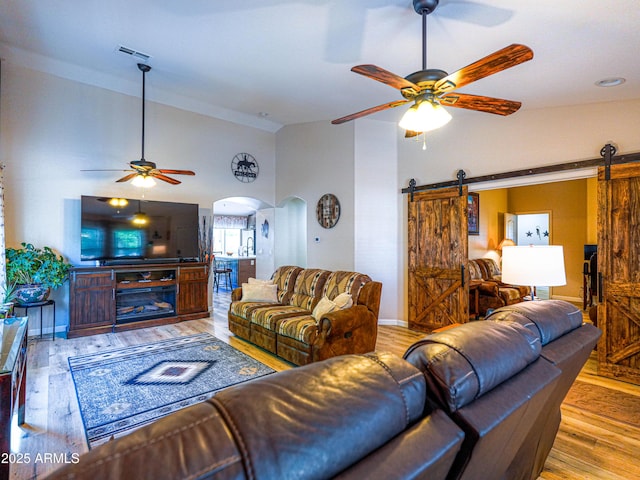 living area with high vaulted ceiling, a barn door, arched walkways, and a ceiling fan