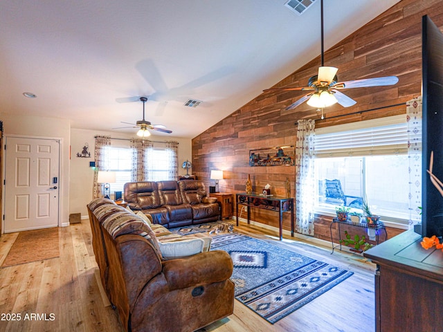 living room with wood finished floors, a ceiling fan, wooden walls, and visible vents