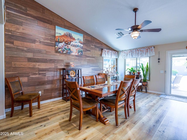 dining space featuring wooden walls, lofted ceiling, visible vents, and light wood finished floors