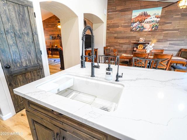 interior space featuring arched walkways, a sink, light wood-style floors, wood walls, and light stone countertops