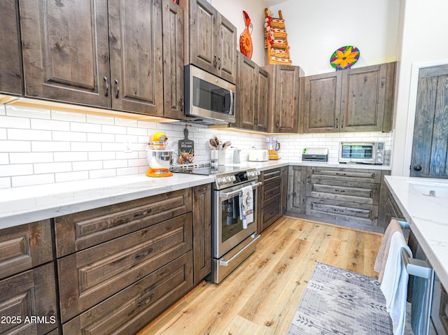 kitchen featuring light stone counters, dark brown cabinets, stainless steel appliances, and light wood-type flooring