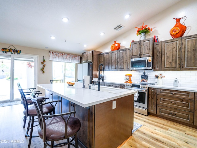 kitchen with a kitchen bar, tasteful backsplash, stainless steel appliances, and light wood-type flooring