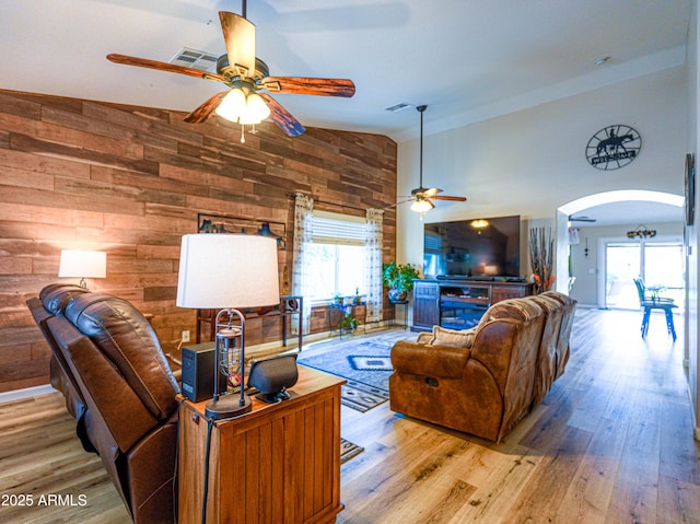 living area featuring arched walkways, ceiling fan, wood walls, and wood finished floors