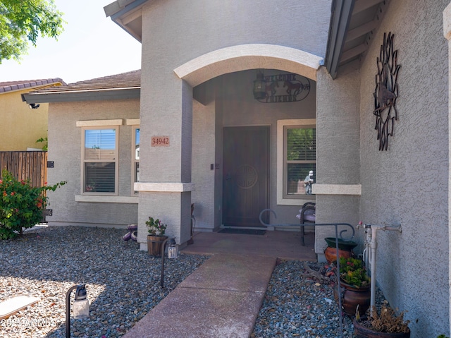 doorway to property featuring stucco siding and fence