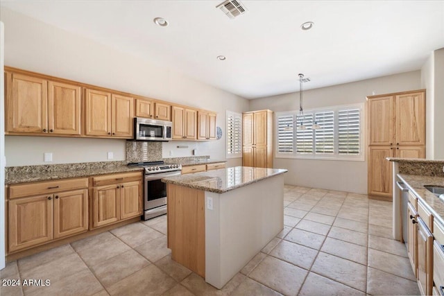 kitchen with light stone counters, appliances with stainless steel finishes, pendant lighting, and a kitchen island