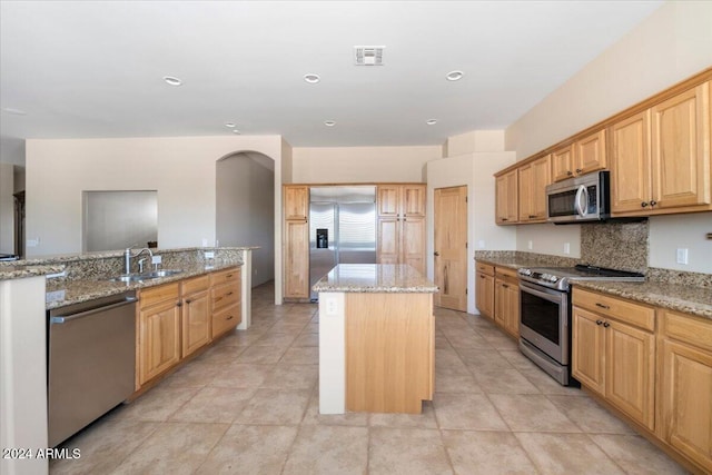 kitchen featuring sink, light tile patterned flooring, a kitchen island, stainless steel appliances, and light stone counters