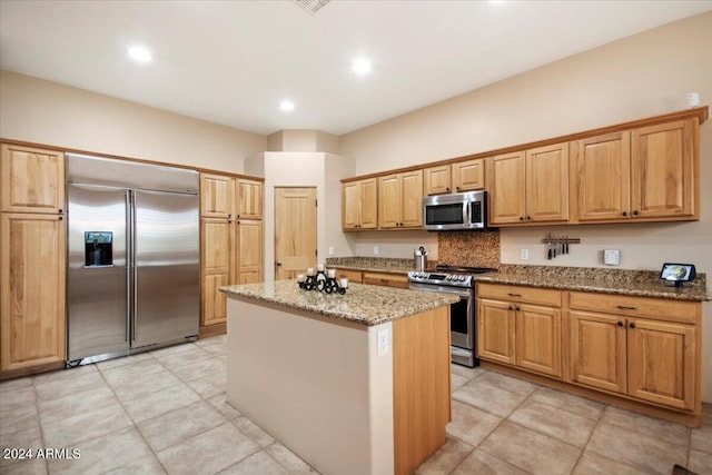 kitchen featuring stainless steel appliances, light tile patterned floors, light stone counters, and a kitchen island