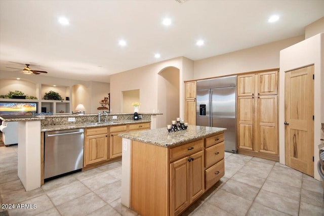 kitchen with appliances with stainless steel finishes, sink, a center island, ceiling fan, and light stone counters