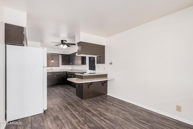 kitchen with freestanding refrigerator, a peninsula, dark wood-style flooring, a ceiling fan, and baseboards