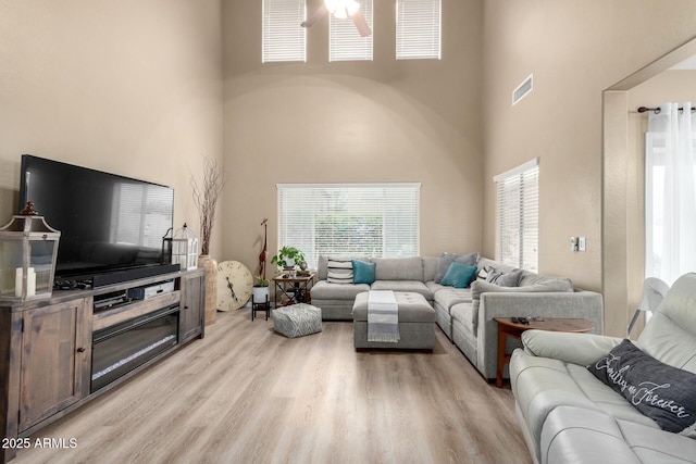 living area featuring visible vents, a high ceiling, ceiling fan, and a healthy amount of sunlight