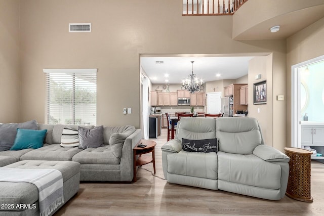 living area featuring an inviting chandelier, a towering ceiling, visible vents, and light wood-type flooring