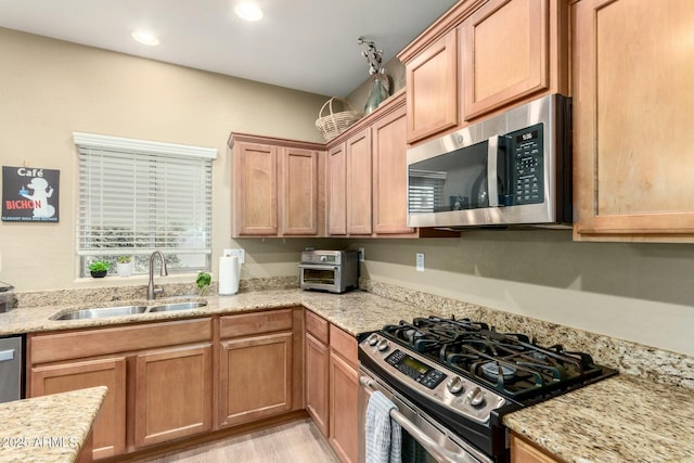 kitchen featuring recessed lighting, light wood finished floors, light stone counters, a sink, and appliances with stainless steel finishes