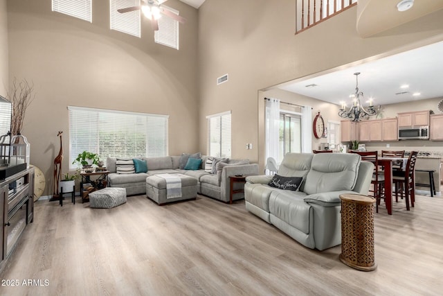 living area with light wood-style flooring, visible vents, a towering ceiling, and ceiling fan with notable chandelier