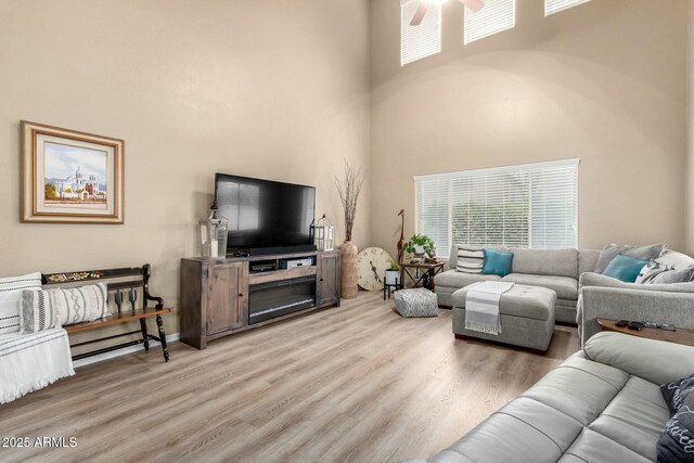 living area with wood finished floors, a high ceiling, a wealth of natural light, and ceiling fan