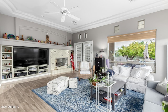 living area featuring wood finish floors, visible vents, a ceiling fan, a tiled fireplace, and a raised ceiling