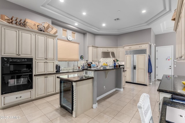 kitchen featuring paneled fridge, wine cooler, under cabinet range hood, dobule oven black, and cream cabinets