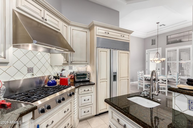 kitchen featuring paneled refrigerator, cream cabinetry, under cabinet range hood, a sink, and stainless steel gas cooktop