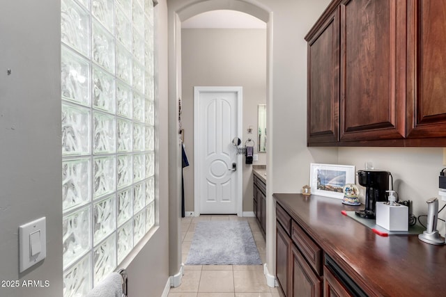 interior space with light tile patterned floors, baseboards, arched walkways, and plenty of natural light