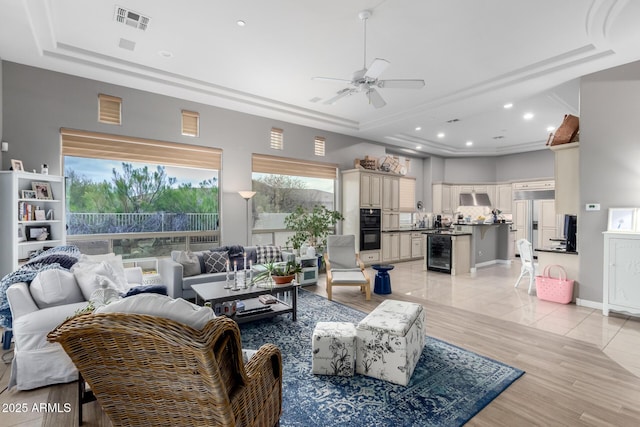 living area with beverage cooler, visible vents, ceiling fan, and a tray ceiling