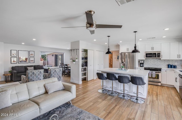 kitchen with a kitchen island, appliances with stainless steel finishes, decorative light fixtures, white cabinetry, and a kitchen bar