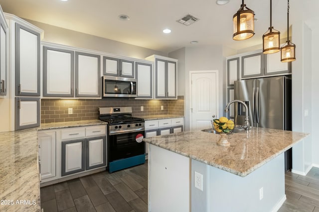 kitchen with appliances with stainless steel finishes, decorative light fixtures, sink, light stone countertops, and a center island with sink