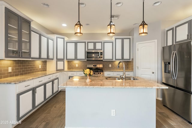 kitchen featuring appliances with stainless steel finishes, pendant lighting, sink, light stone counters, and a center island with sink