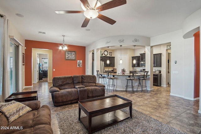 tiled living room featuring ceiling fan with notable chandelier