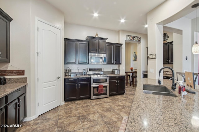 kitchen featuring sink, hanging light fixtures, light stone counters, tile patterned floors, and appliances with stainless steel finishes