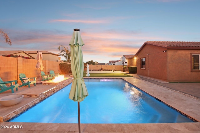 pool at dusk with a fire pit, a patio area, and pool water feature