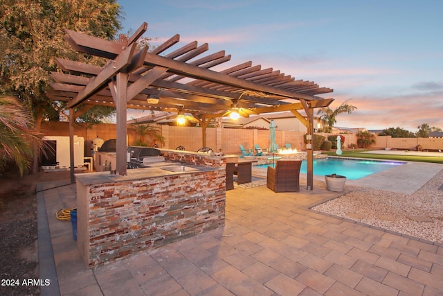 pool at dusk with area for grilling, a pergola, a patio, and exterior kitchen