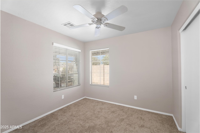 carpeted spare room featuring baseboards, visible vents, and ceiling fan