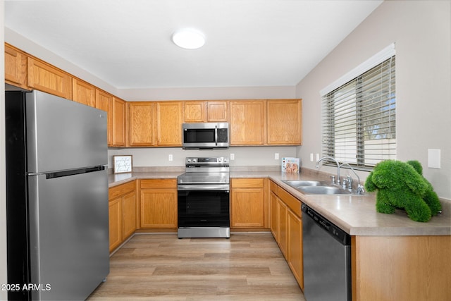 kitchen featuring appliances with stainless steel finishes, light countertops, a sink, and light wood finished floors