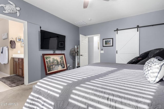 bedroom with light carpet, connected bathroom, a barn door, and ceiling fan