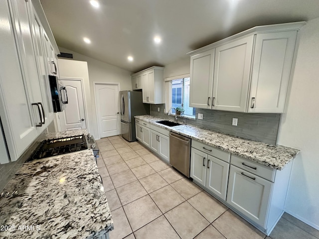 kitchen featuring light stone counters, lofted ceiling, a sink, stainless steel appliances, and tasteful backsplash