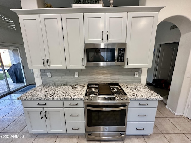 kitchen with backsplash, light stone counters, appliances with stainless steel finishes, arched walkways, and white cabinets