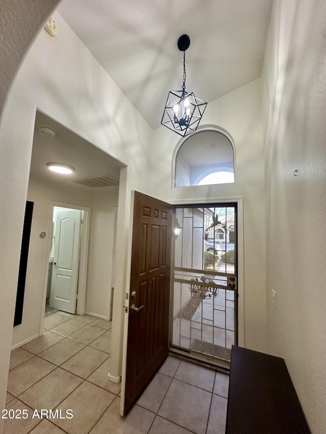 foyer entrance with a notable chandelier, a high ceiling, light tile patterned floors, and baseboards