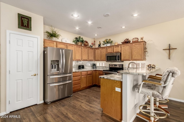 kitchen featuring kitchen peninsula, appliances with stainless steel finishes, light stone countertops, dark hardwood / wood-style floors, and a breakfast bar area