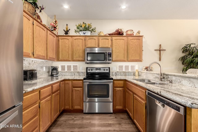 kitchen with kitchen peninsula, appliances with stainless steel finishes, dark hardwood / wood-style flooring, light stone counters, and sink