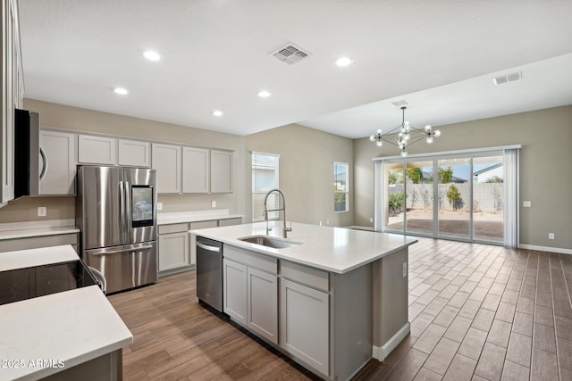 kitchen with pendant lighting, sink, a notable chandelier, stainless steel appliances, and a center island with sink