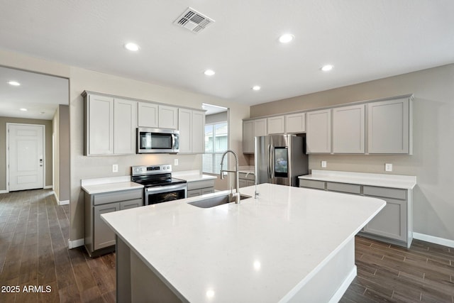 kitchen featuring an island with sink, stainless steel appliances, gray cabinets, and sink