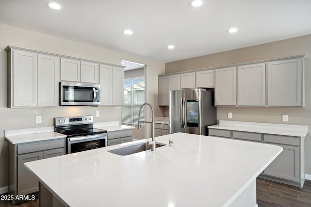 kitchen with stainless steel appliances, an island with sink, sink, and gray cabinets