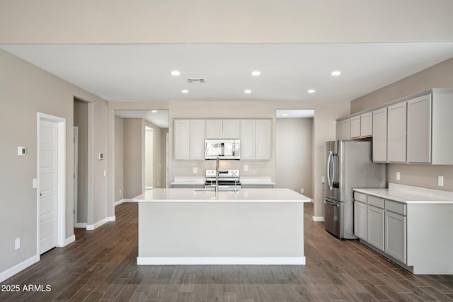 kitchen with stainless steel appliances, dark hardwood / wood-style flooring, and a center island with sink